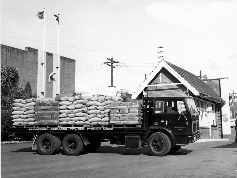 Flatbed of McCaffery Services Pty Ltd, laden with bagged sugar, departs refinery, circa 1960